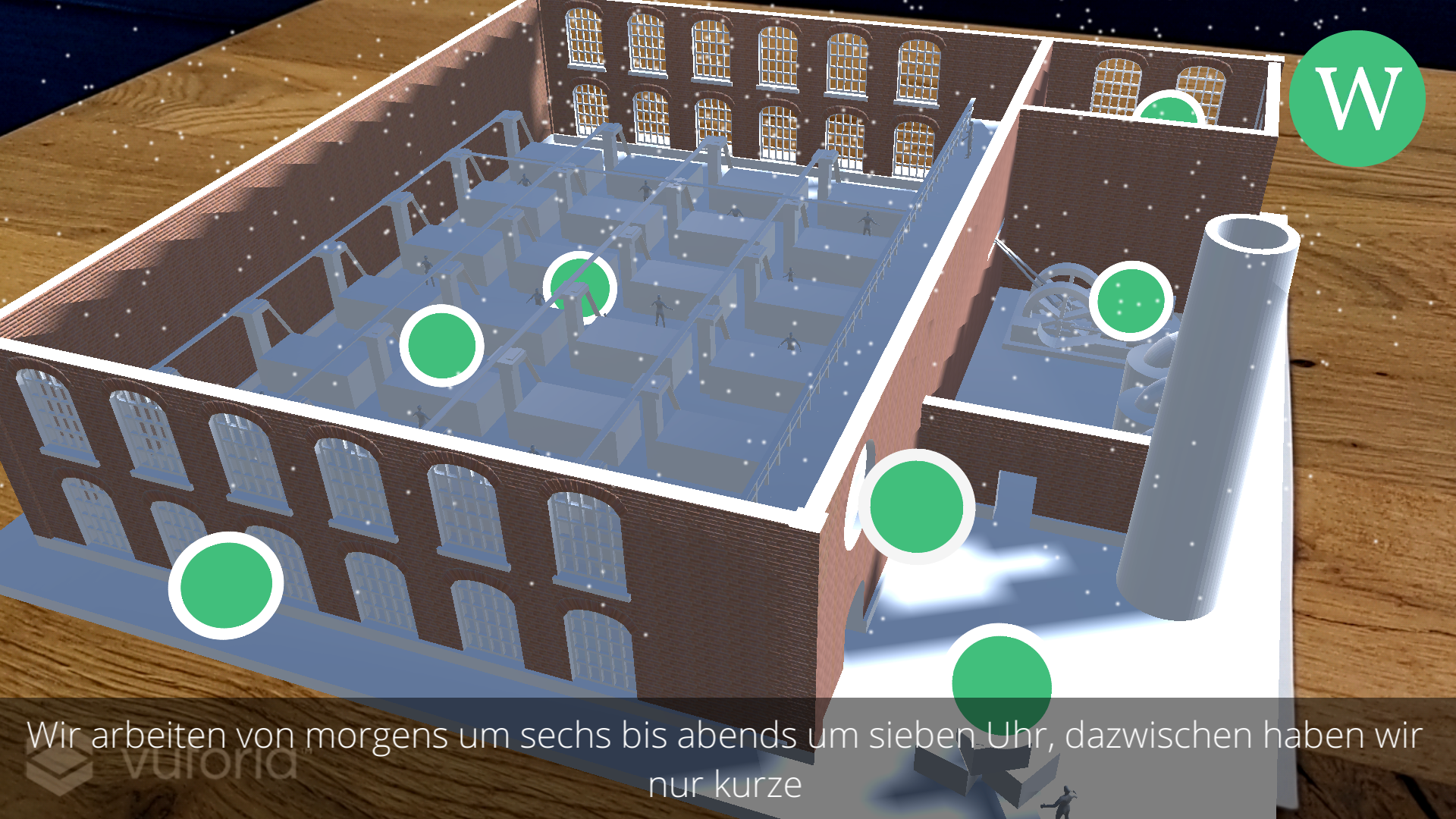 Screenshot of yARn that shows a 3D rendered factory projected on a wooden table from the perspective of the weaver. There are several green colored points of interest inside the factory. At the bottom of the screen subtitles are displayed.